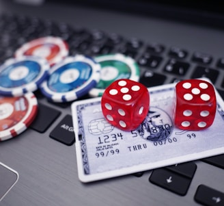 A set of red dice and poker chips are placed on top of a credit card, which is situated on a laptop keyboard. The poker chips are in various colors, including blue, green, red, and white.