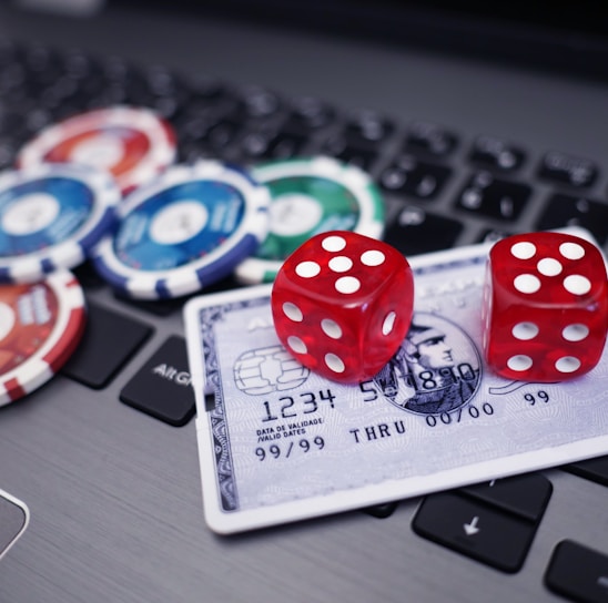 A set of red dice and poker chips are placed on top of a credit card, which is situated on a laptop keyboard. The poker chips are in various colors, including blue, green, red, and white.