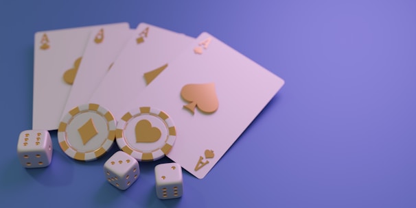 A set of playing cards displaying four aces is laid out on a surface. Alongside them, there are two poker chips with heart and diamond symbols, and three six-sided dice showing different numbers. The background is a smooth gradient of purple, creating a thematic gaming or casino atmosphere.