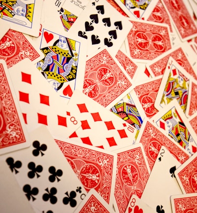 A vibrant assortment of playing cards scattered in a chaotic manner. The cards display various suits and numbers, predominantly featuring the colors red and black with intricate designs. Several face cards are visible, showcasing traditional royal characters in vivid detail.